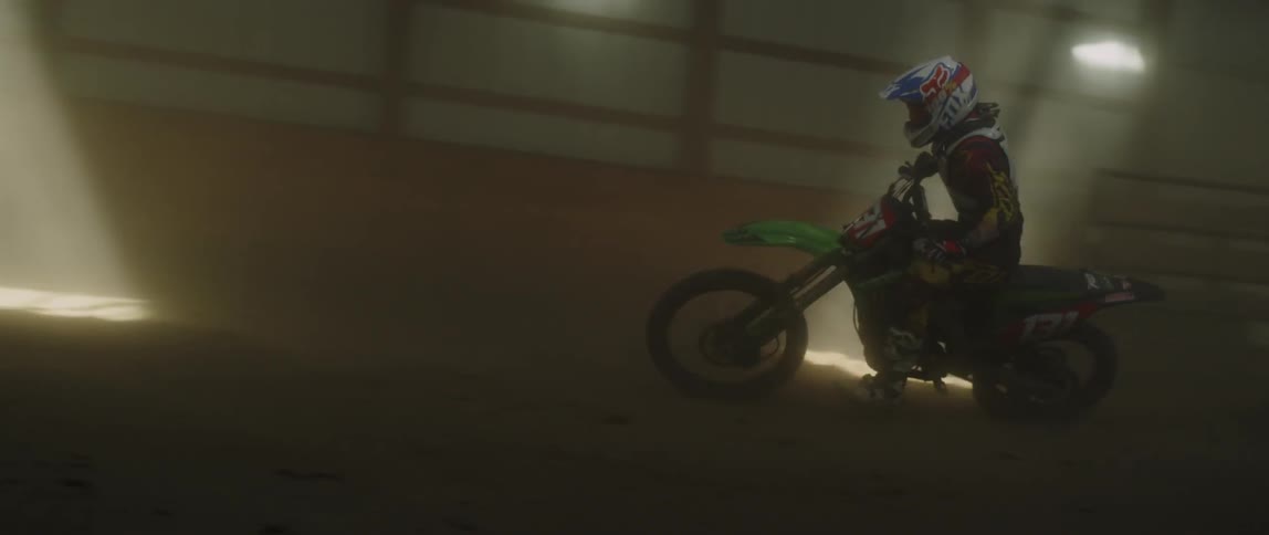 A man drives a dirt bike inside a dirt arena