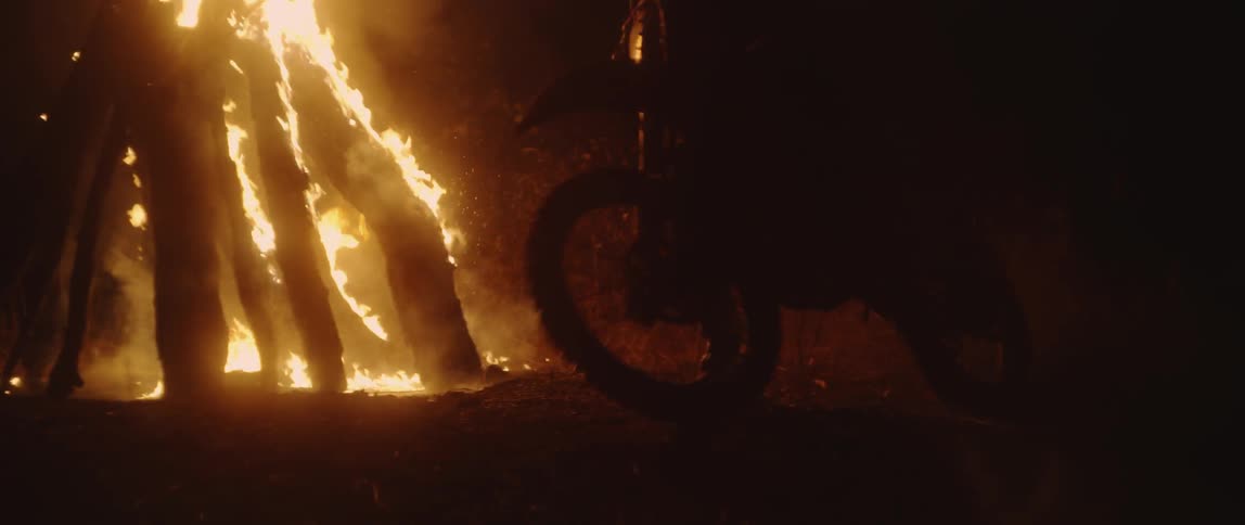A person rides a dirt bike around a bonfire