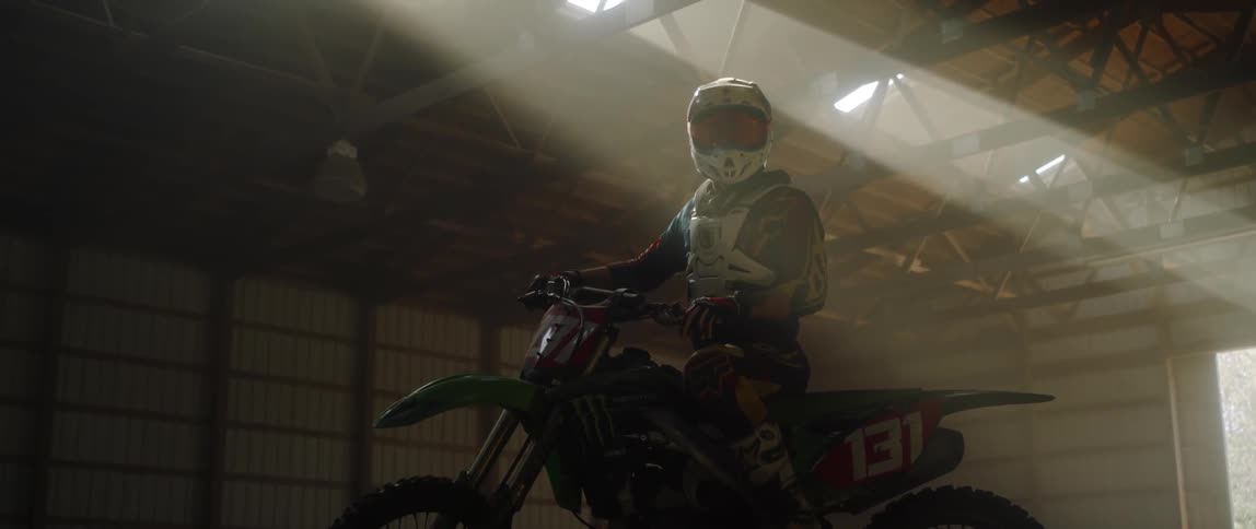 A man sits on a dirt bike in an indoor arena
