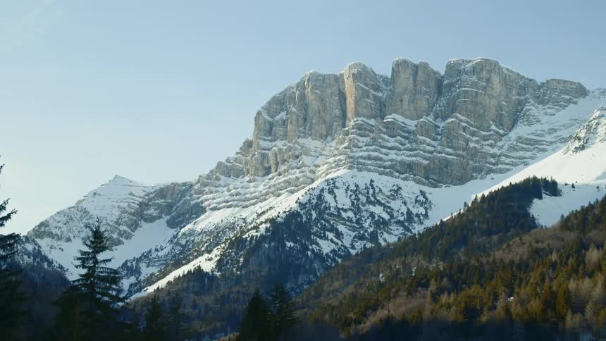 Snow covers the slopes and crags of a cliff on a sunny day