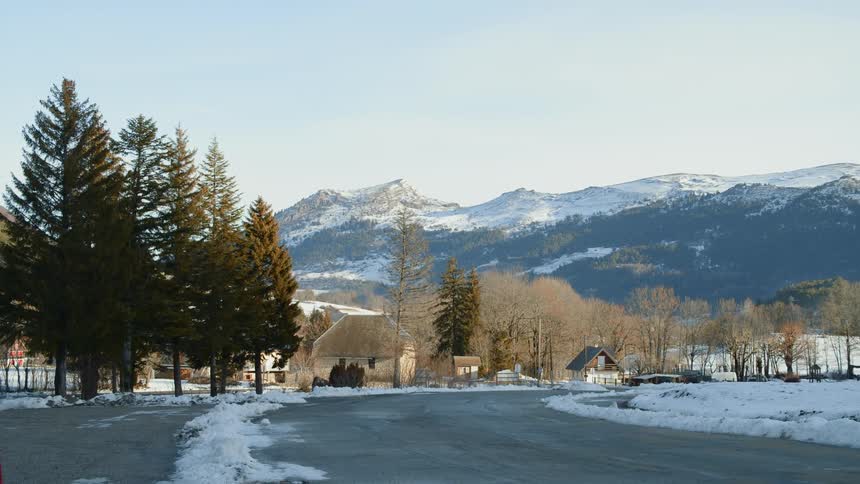 Country road lined with buildings and trees and mountains in the distance