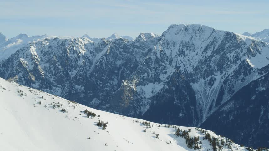 A snow covered mountain side is filming other snow covered mountains in the distance