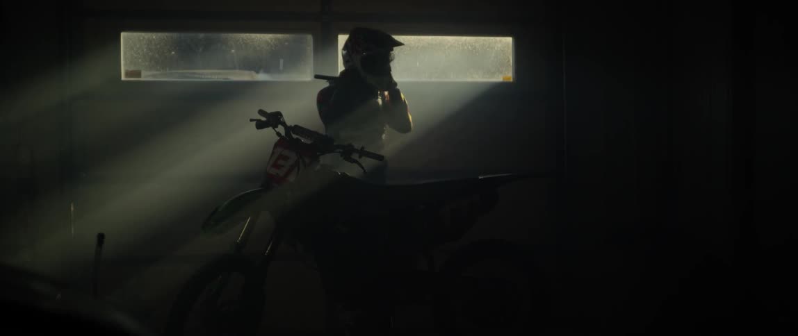 Person puts on a helmet and sits on a dirt bike in a garage