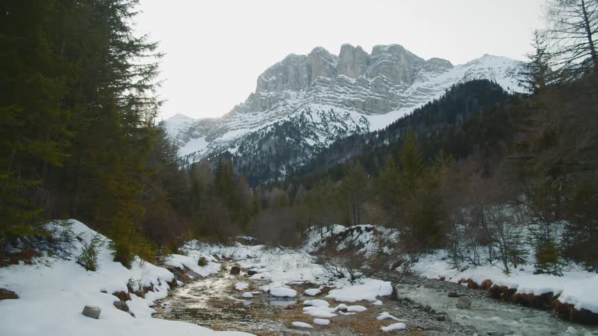 Stream flows through rocky snow covered land surrounded by hills