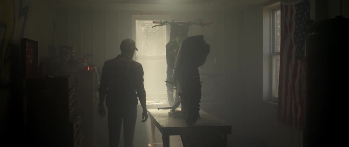 A man walks into a garage with a dirt bike on a table