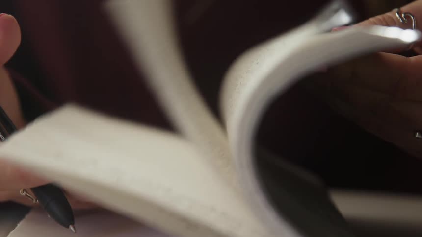 A woman is flipping through the pages of a writing notebook inside in daylight