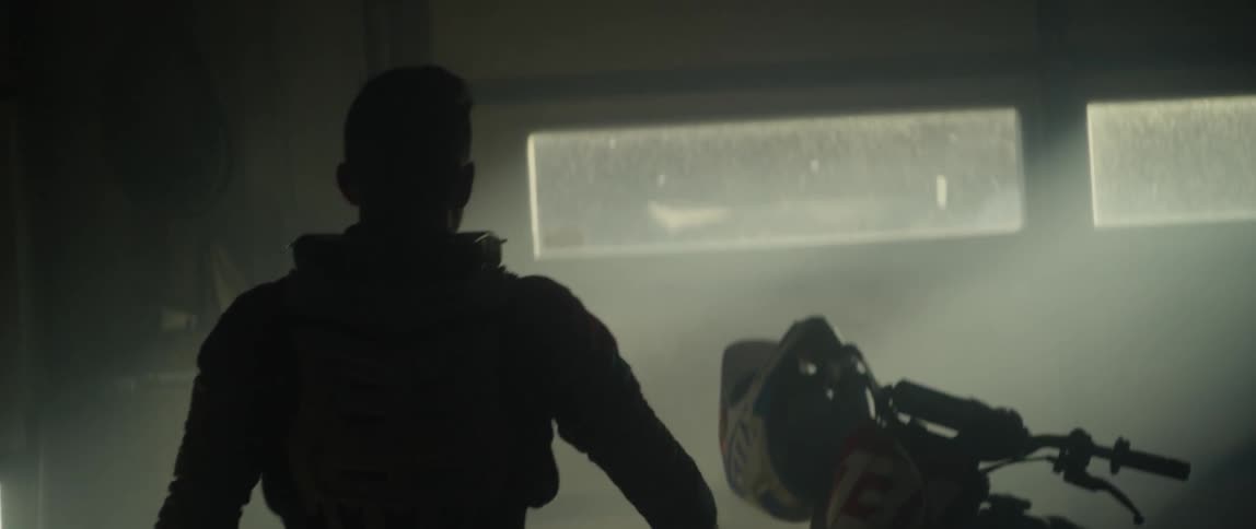 A man walks towards a dirt bike in a garage