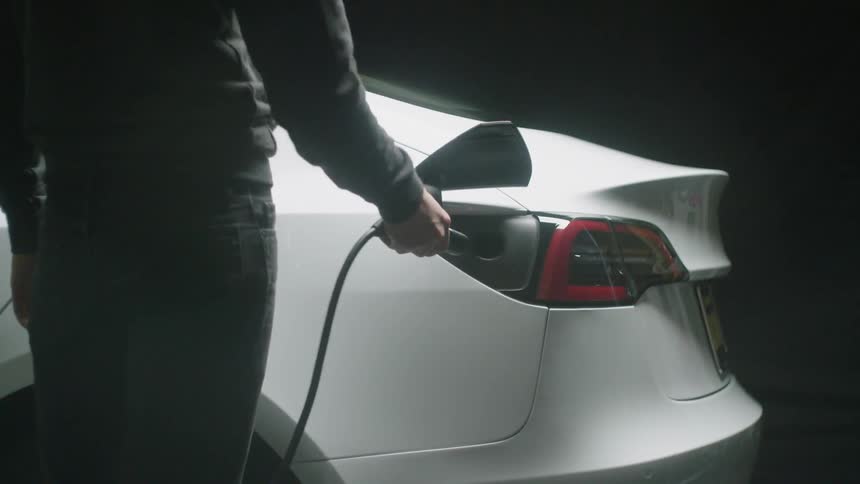A man plugs a cord into a white electric car