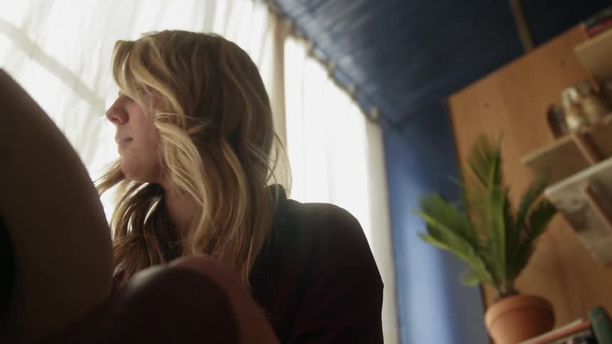 A woman sitting at a table in a home in daylight is turning to look out a window