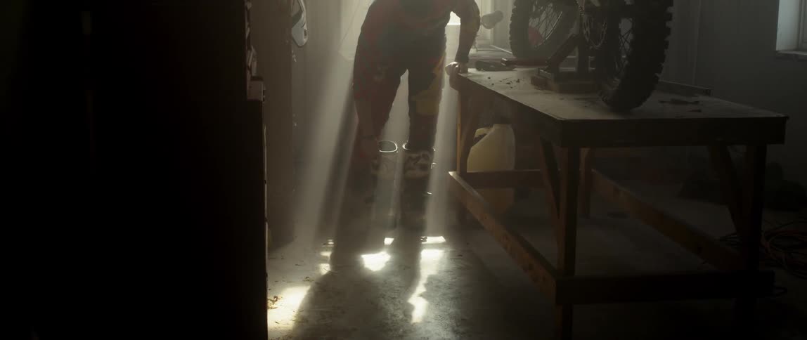 A man standing inside in daylight is putting on dirt bike boots