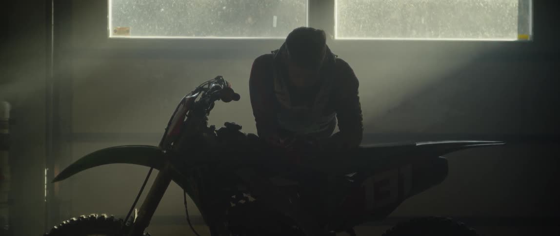 A man leans on a dirt bike in a garage