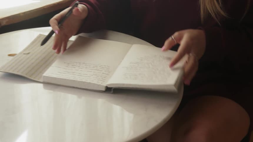 A woman writes in a notebook at a small table
