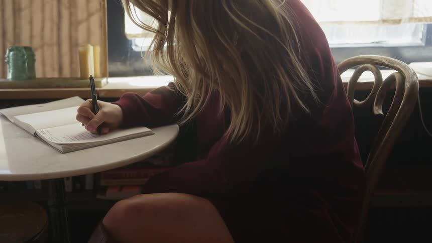 A woman writes in a notebook at a small table