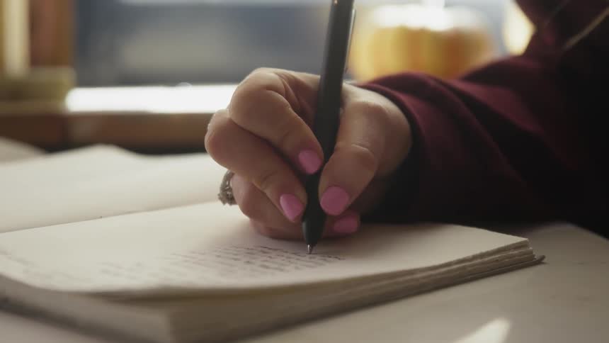 A woman is writing poetry in a notebook inside in daylight