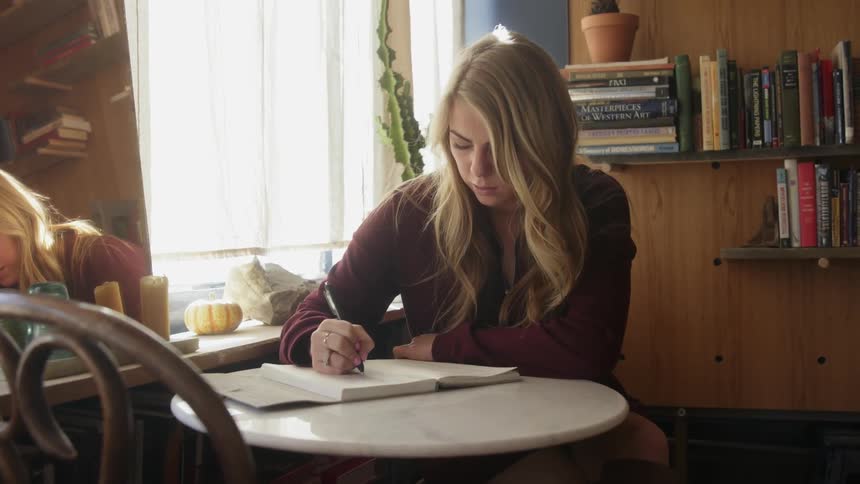 Woman sits at a table writing in a notebook