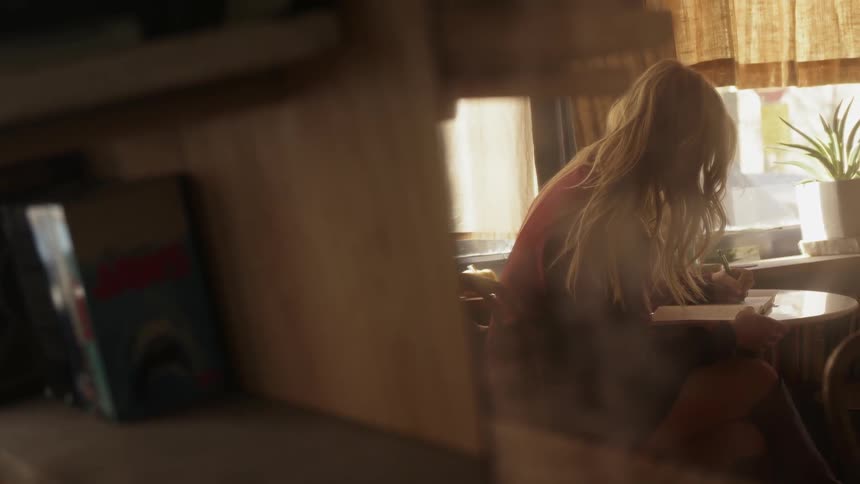 Woman sits at a table writing in a book