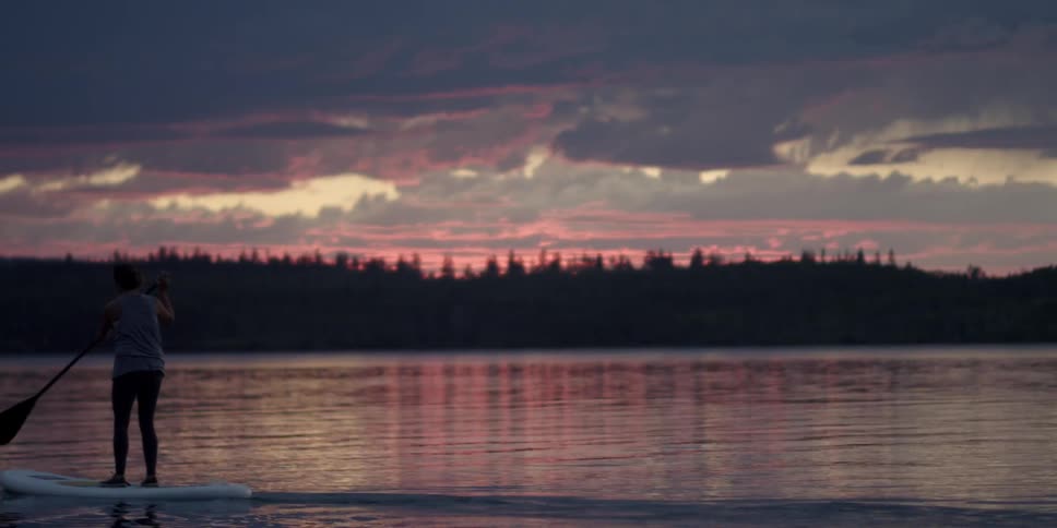 A woman paddle boards on a lake at sunset
