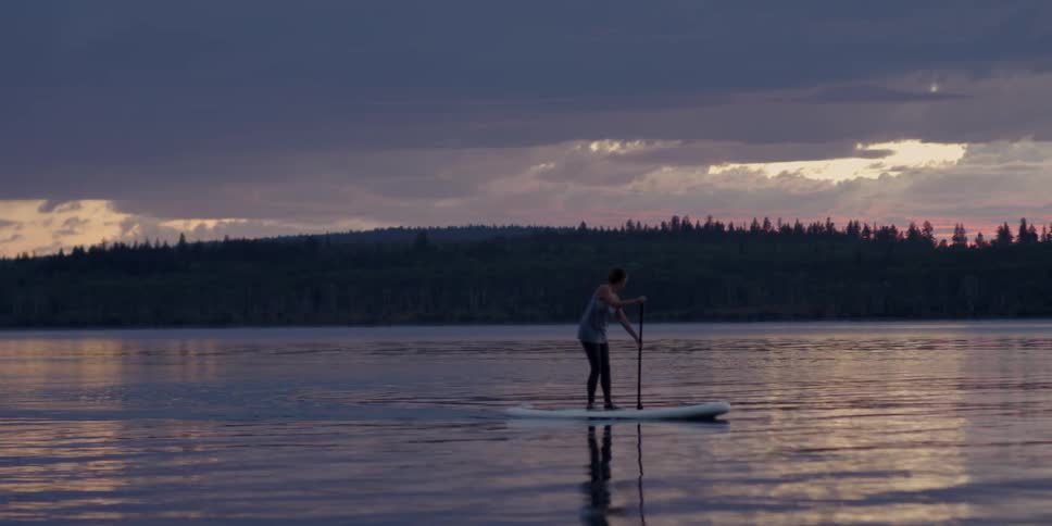 Person paddle boarding on calm waters near a cloudy sunset