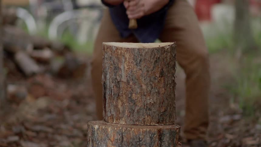 Man is chopping block of wood in half with ax