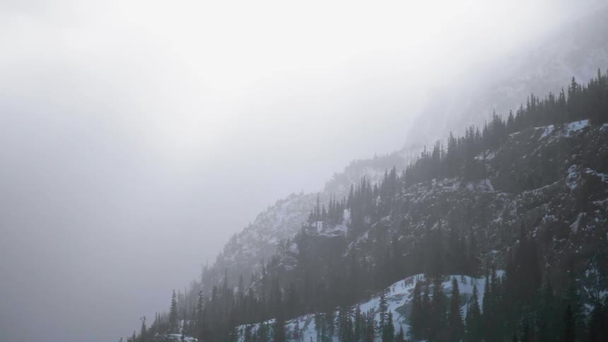 Snow flurries are blowing across a mountainside during the day