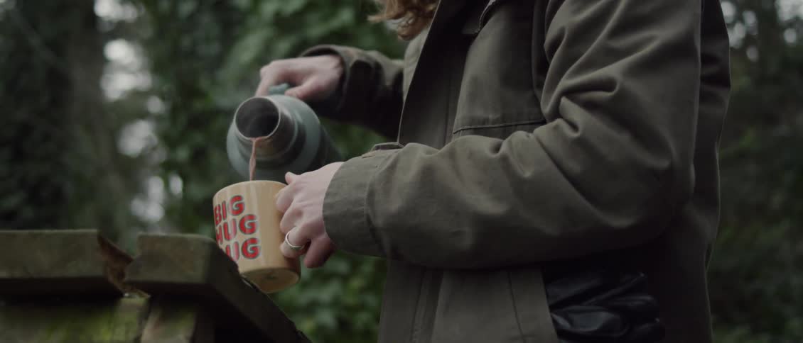 Person pours liquid from a thermos into a mug outside