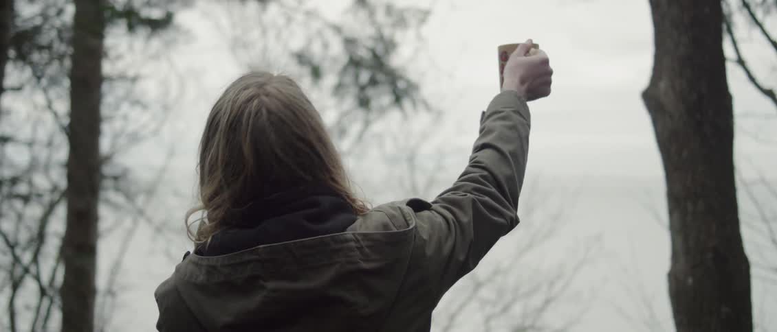 Man standing outside on a cloudy day raises his mug over his head
