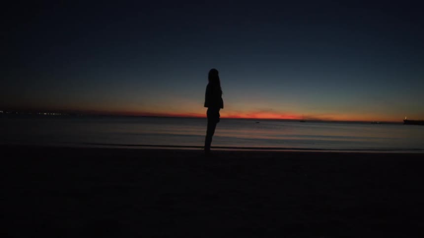 A woman stands on the beach at sunset