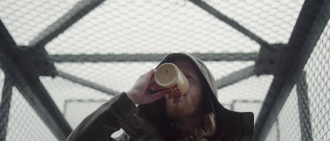 A man is drinking a cup of coffee as he walks across a bridge in daylight