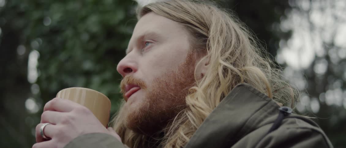 A man standing outside blows on his hot drink and sips