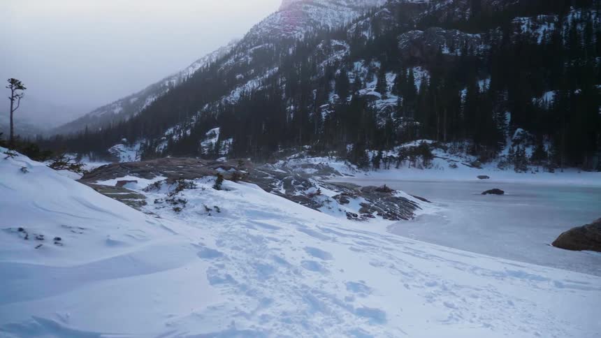 Snow falls on the frozen lake at the foot of a mountain