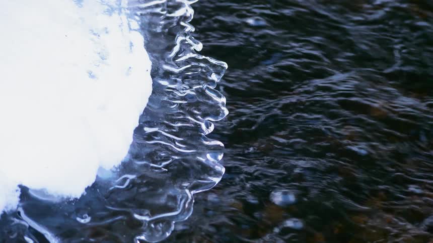 Water flows underneath melting ice and snow on a sunny day