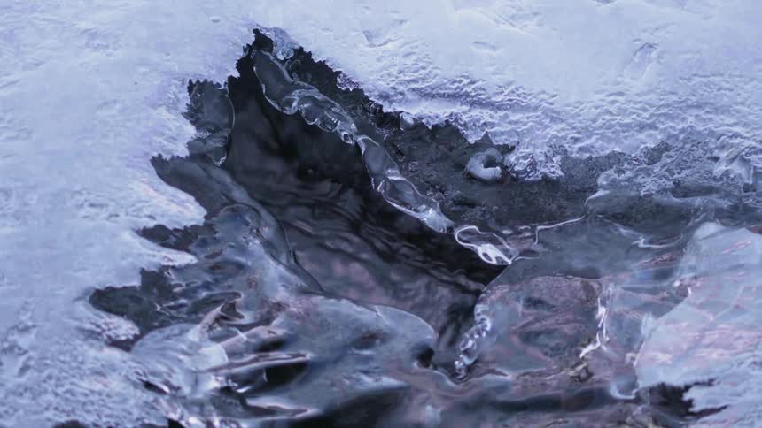 Water is flowing under melting ice in a natural setting in daylight