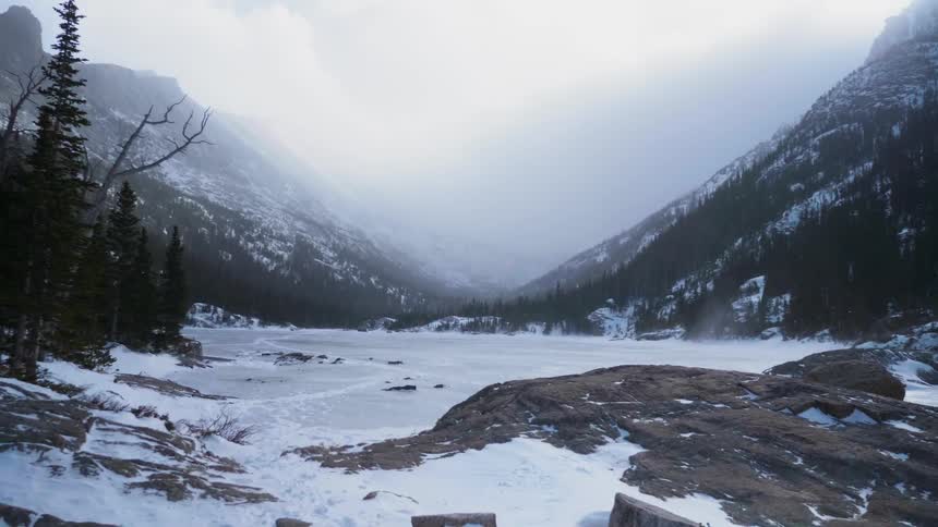 Snow falls on the frozen lake at the foot of a mountain