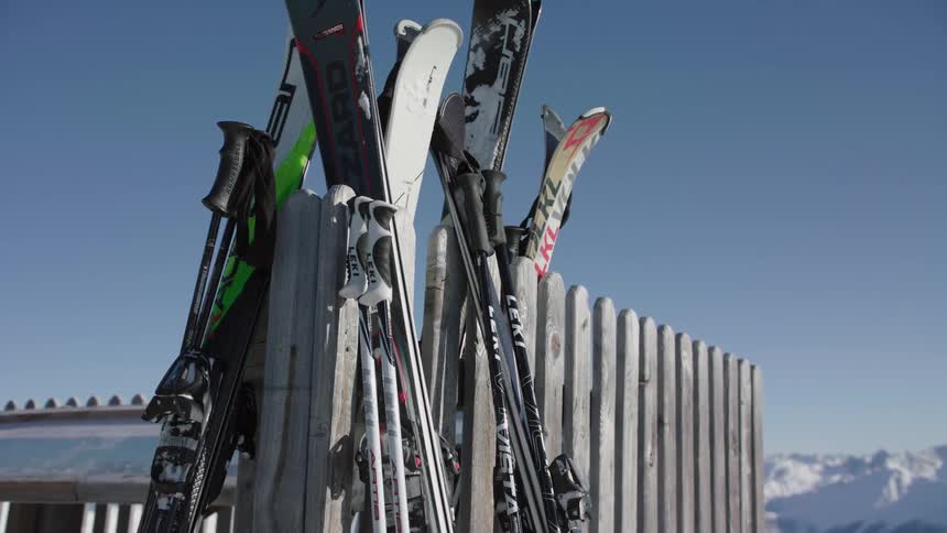 Skis are leaning against a fence at a ski resort on a sunny day