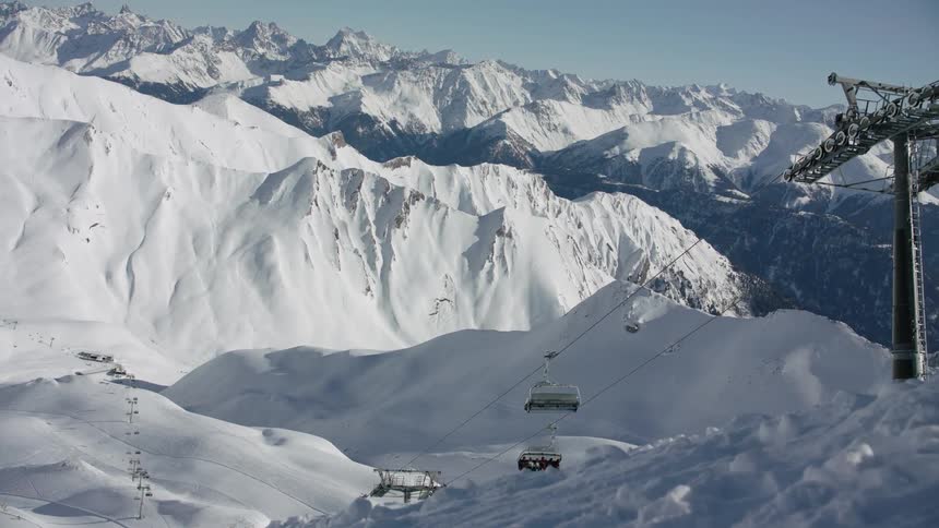 Skiers are traveling on a ski lift in a mountain range on a sunny day