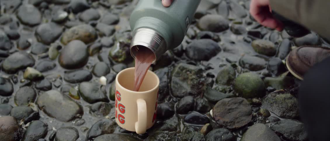 Person pours liquid from a thermos into a mug outside