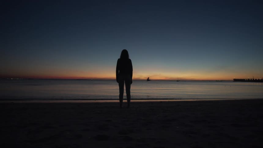Person stands on the beach at sunset looking out