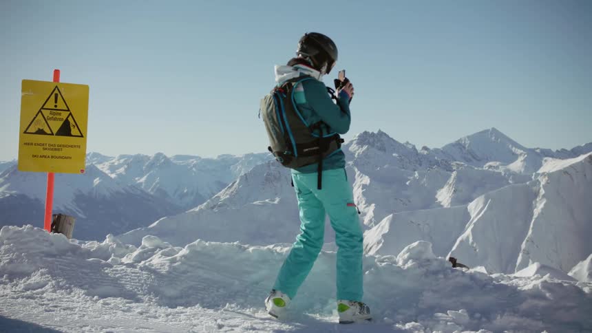 A skier takes a photo with their phone atop a mountain