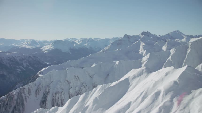 Skis and snowboards lean against a rail overlooking snow covered peaks