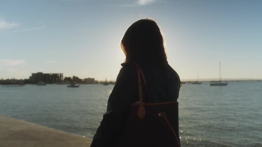 A woman walks near the ocean on a cement pier