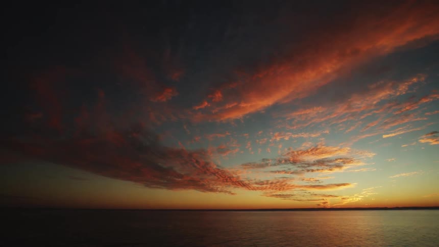 Colorful sunset occurring behind clouds in the distance before a large body of water