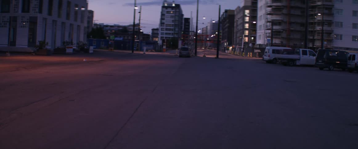 A desolate city road sits quietly near dark residential buildings during late evening