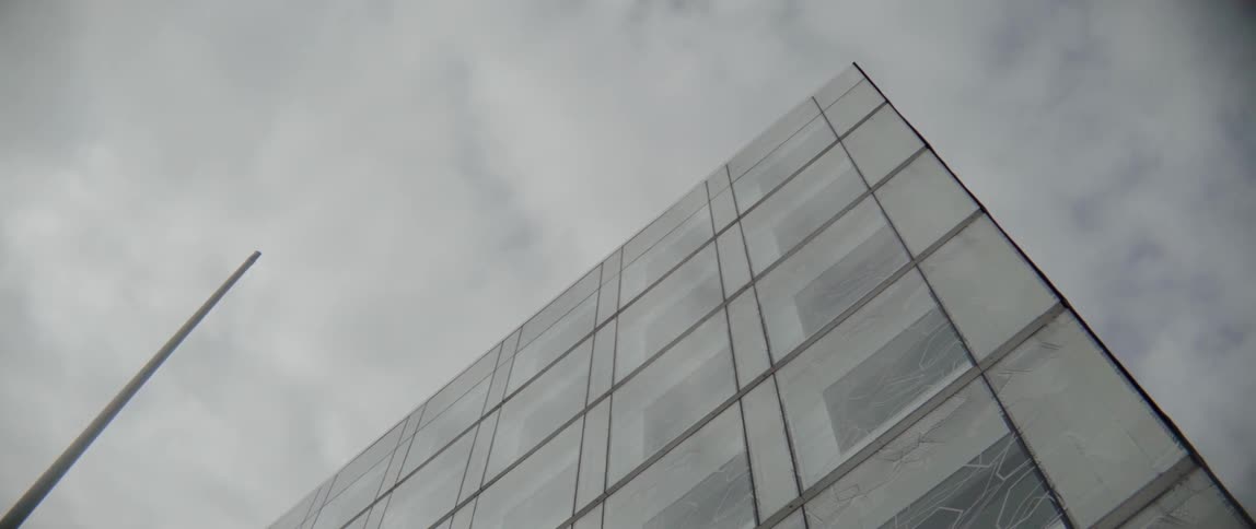Sleek glass windows create sharp diagonal lines against a cloudy metropolitan background alone.