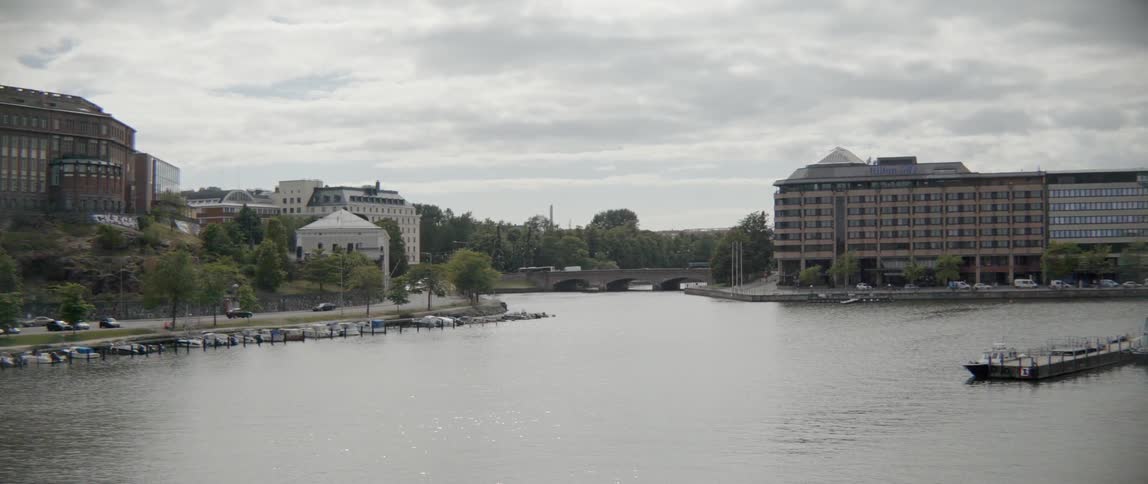 A peaceful river runs past residential districts and city architecture under grey skies.