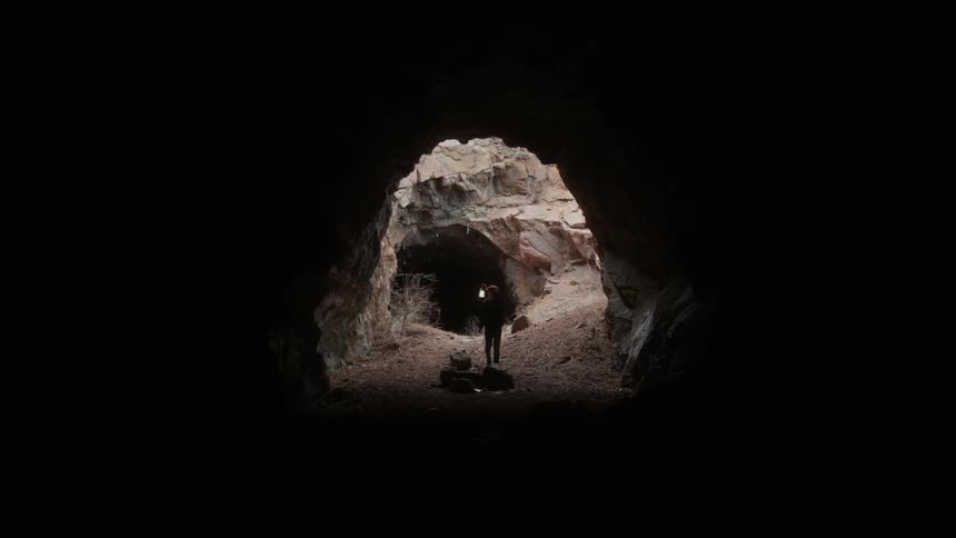 Man is walking through a dark cave holding lantern