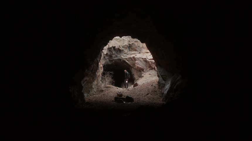 Man holding lantern is standing near the entrance of dark cave