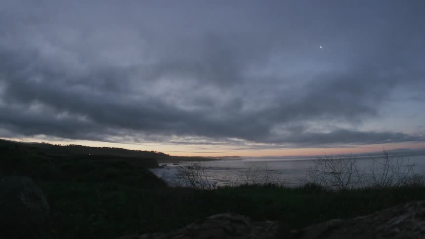 Time lapse of storm clouds moving over and past a coastal area at sunrise