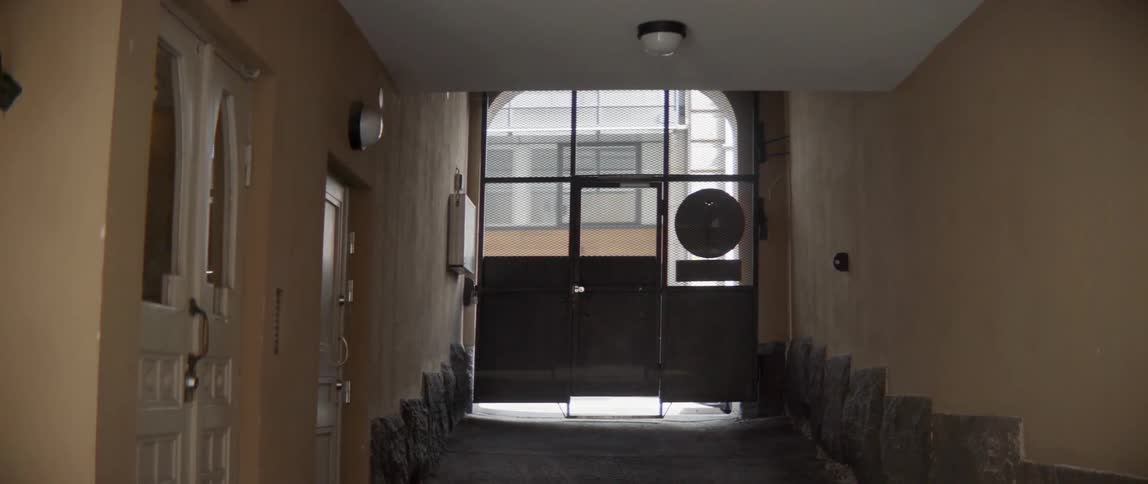 A dark apartment building passageway opens up to a bright outdoor street scene.