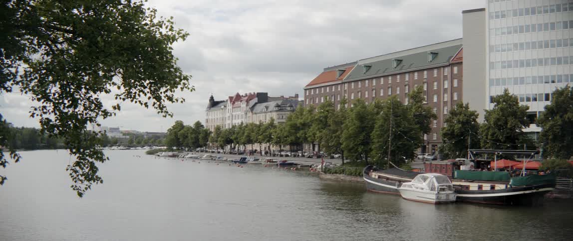 Several vessels sit docked on a quiet metropolitan waterway under cloudy summer skies.