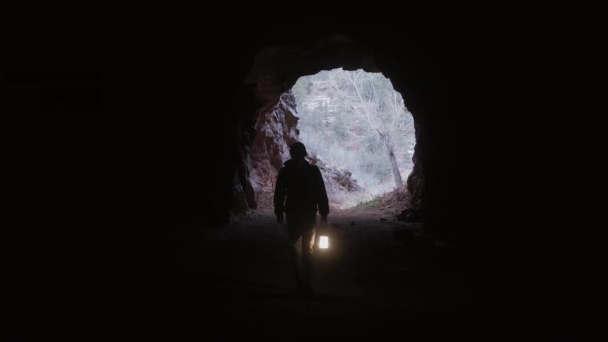 A man walks into a cave holding a lantern